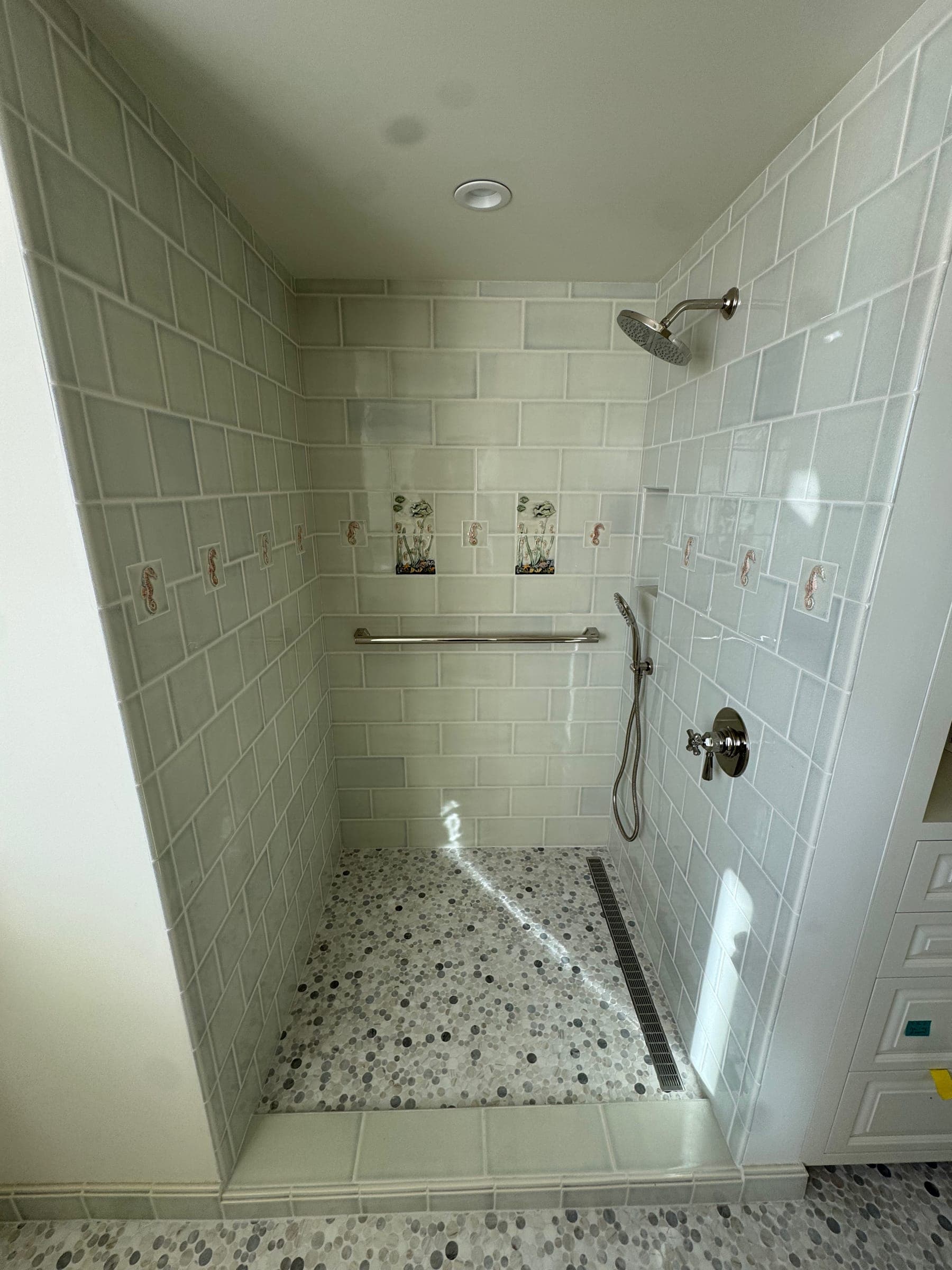 Custom walk-in shower with hand-painted accent tiles and pebble mosaic floor