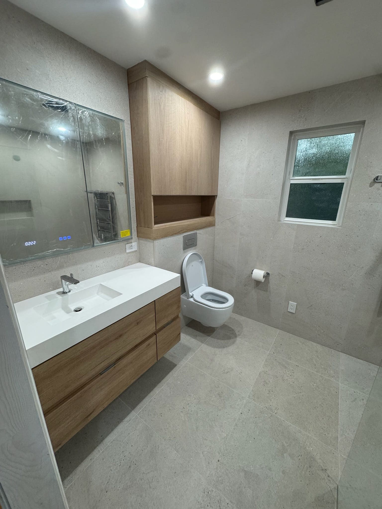 Finished master bathroom with floating oak vanity, wall-hung toilet, and custom oak cabinets above