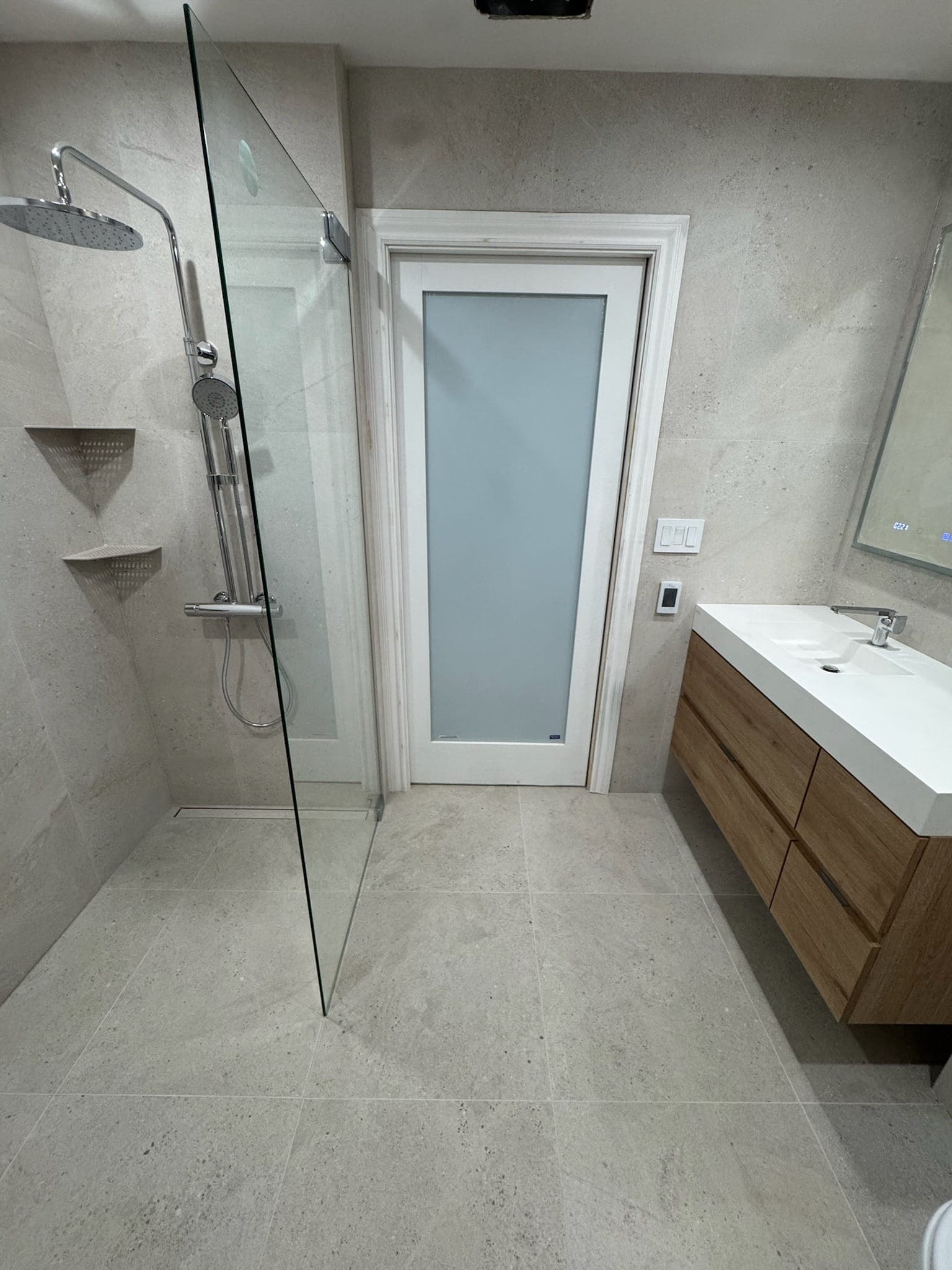 Finished master bathroom with glass shower panel, frosted pocket door, and floating oak vanity