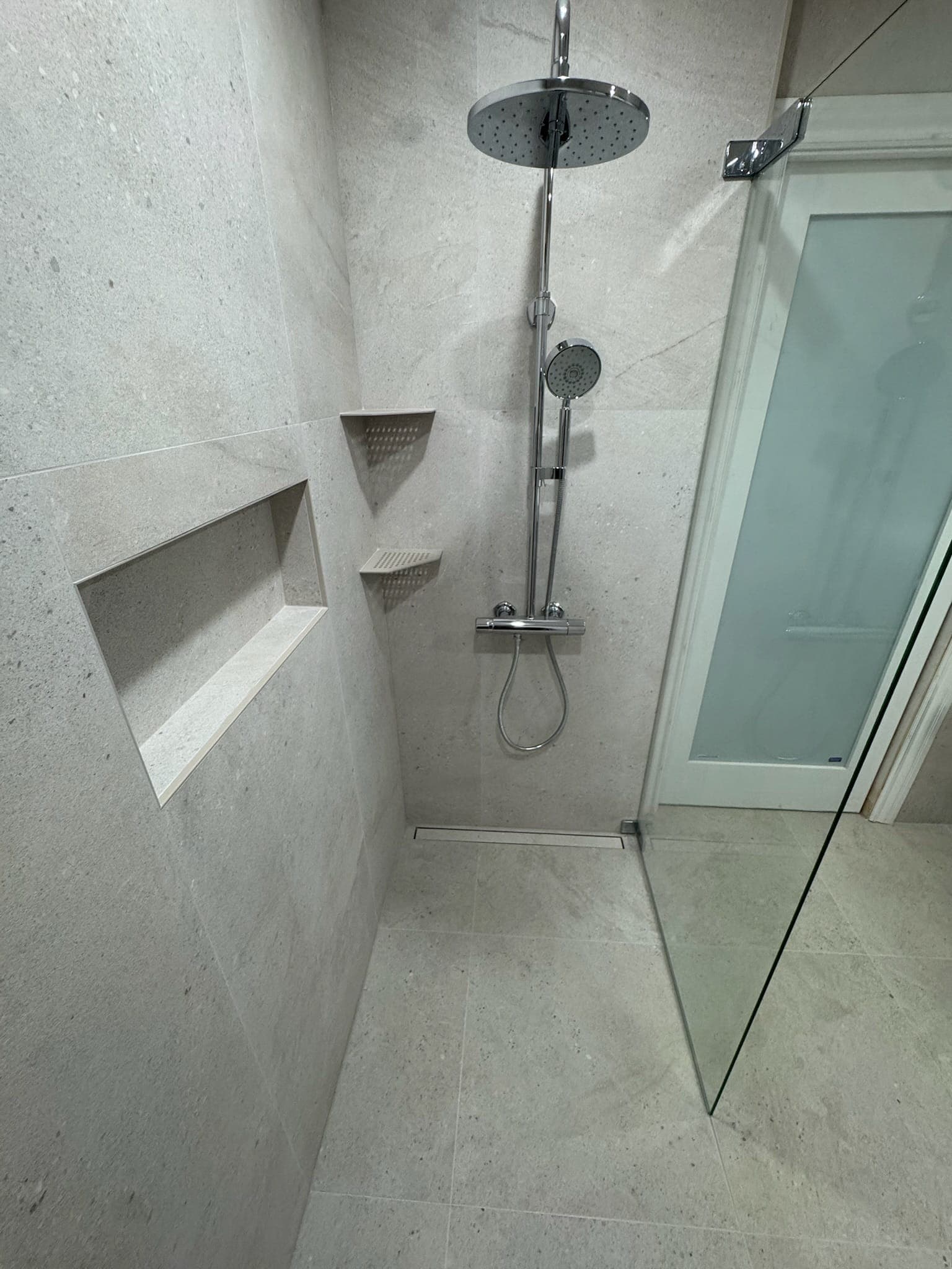 Completed curbless shower with thermostatic rain column, handheld sprayer, and glass panel