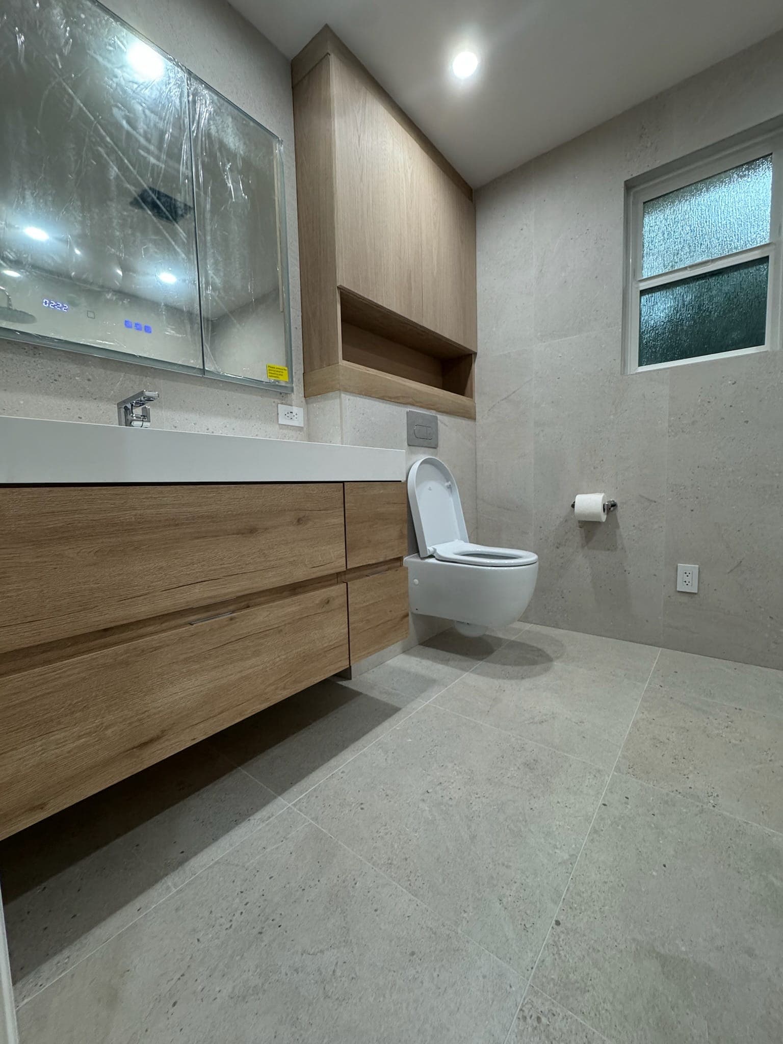 Floating oak vanity and wall-hung toilet below custom oak cabinetry in the finished bathroom