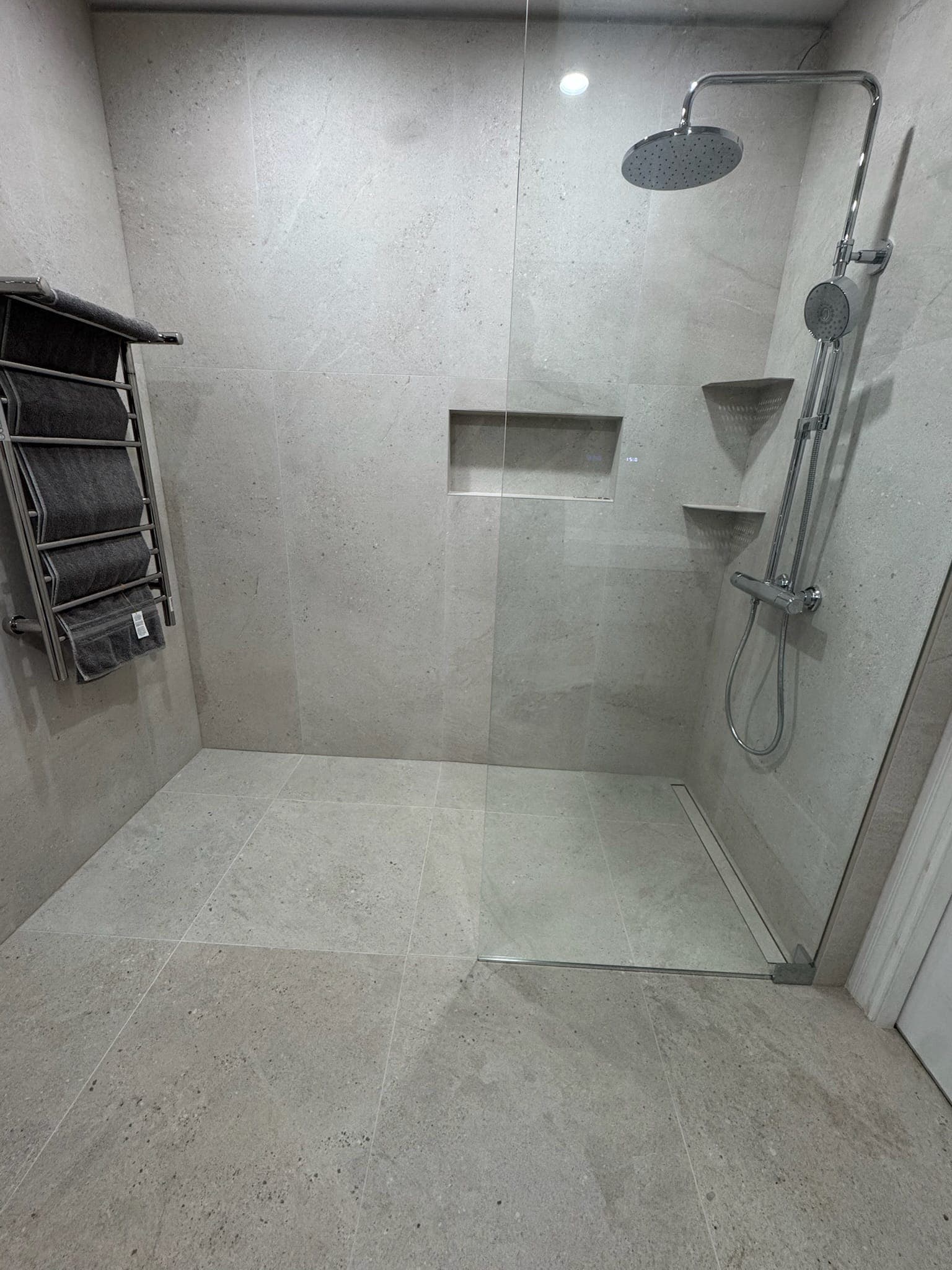 Completed walk-in shower with rain column, tiled niche, and heated towel rack